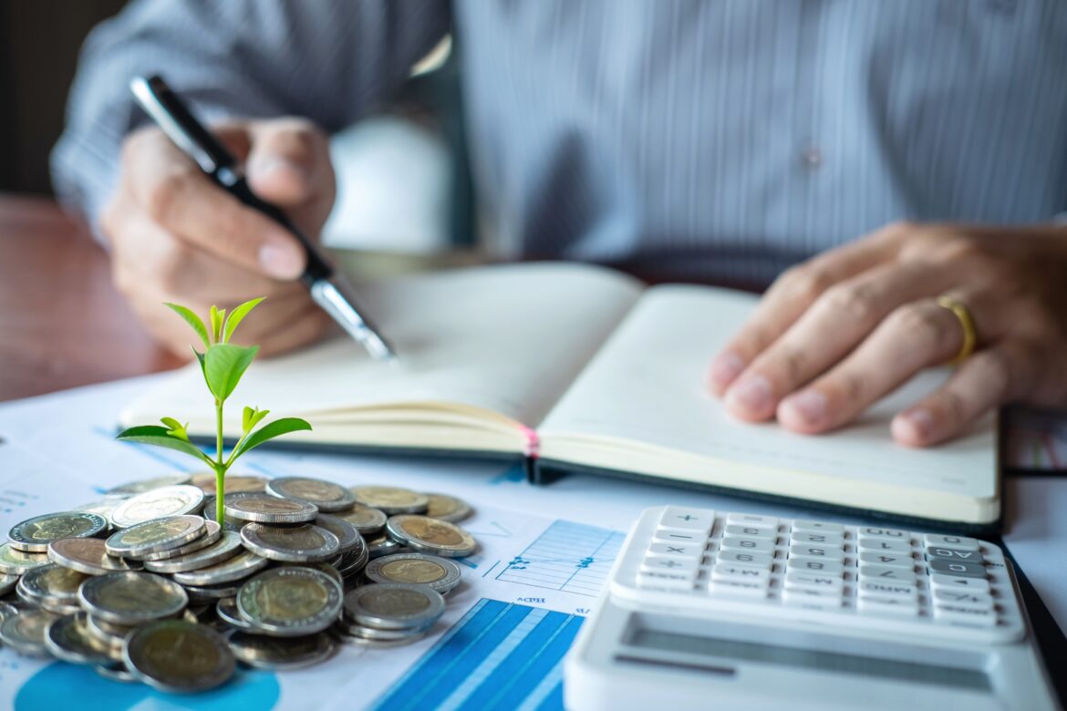 Pound-cost averaging: man writing in a book with coins and shoot on his table
